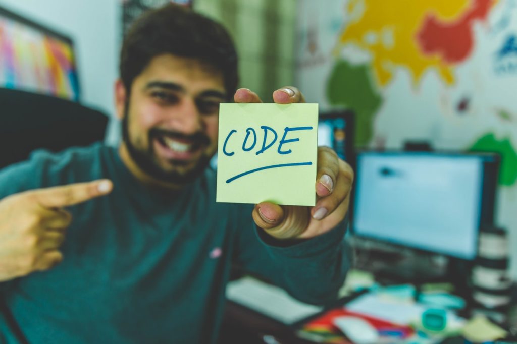 Man in green sweater holding a stick note with code on it