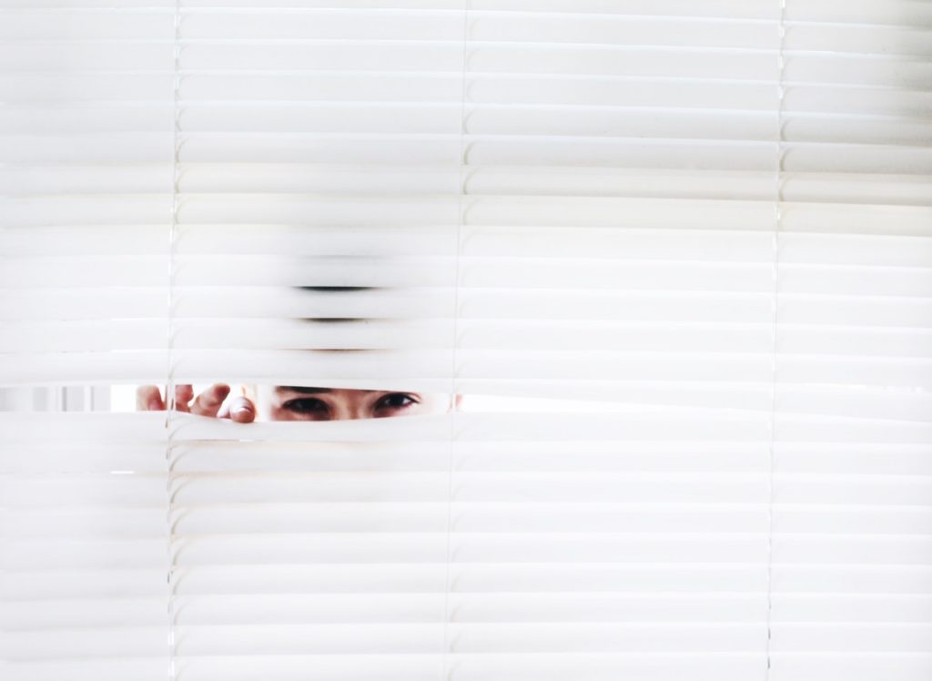 Man peering through white blinds