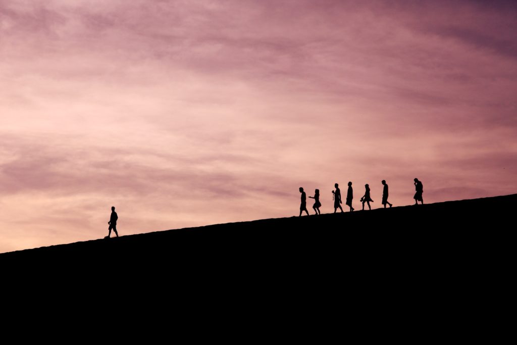 One person leading a group down a hill at sunset