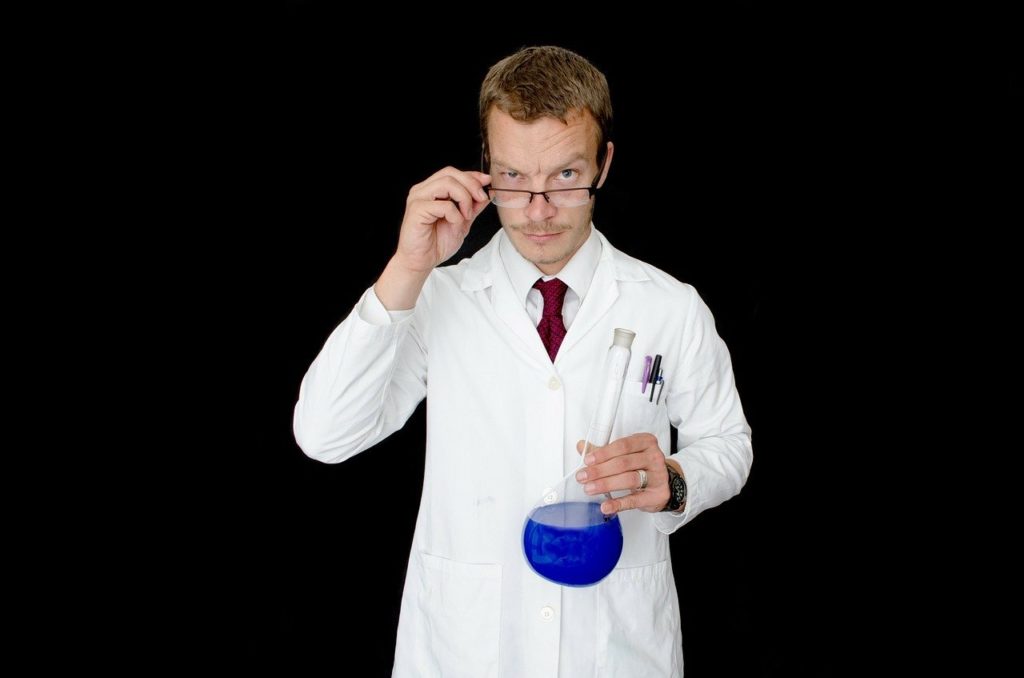 Man in white lab coat with glass vessel in hand