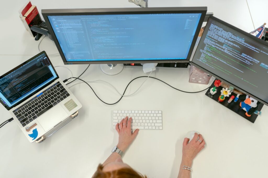 Overhead of woman coding with macbook and monitors
