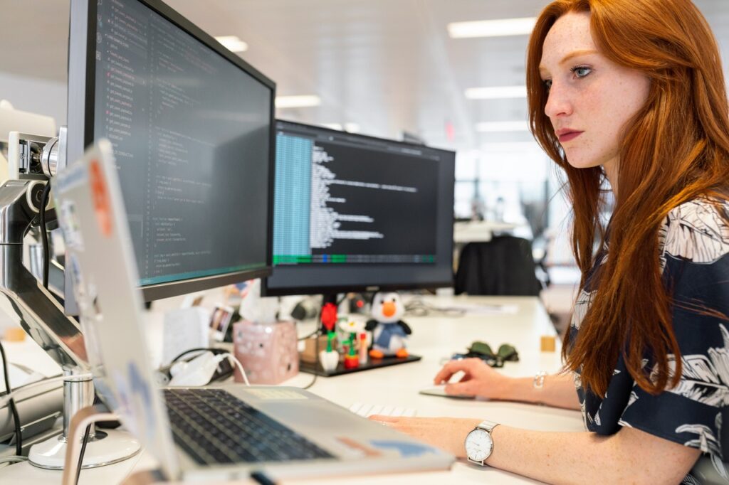 Woman in front of computer monitors coding